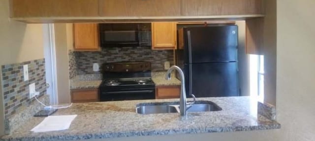 kitchen featuring black appliances, tasteful backsplash, sink, and light stone countertops