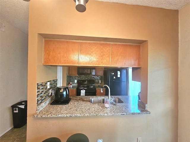 kitchen with light stone counters, sink, black appliances, tasteful backsplash, and a textured ceiling