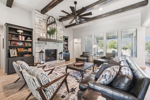 living room featuring beamed ceiling, ceiling fan, a stone fireplace, and light wood-type flooring