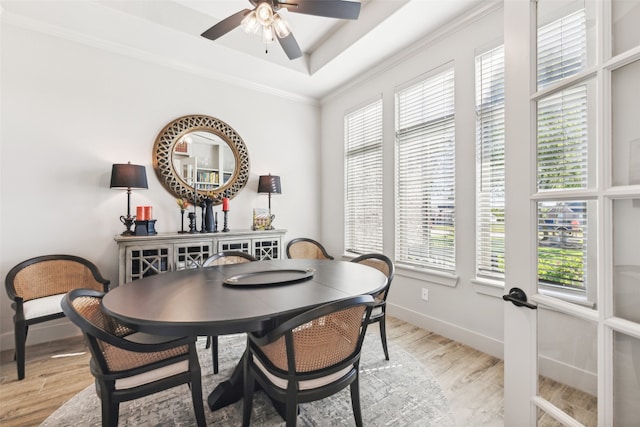 dining area with a raised ceiling, light wood-style flooring, a ceiling fan, ornamental molding, and baseboards