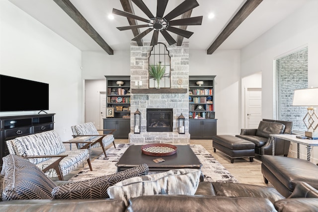 living room featuring beam ceiling, a stone fireplace, wood finished floors, and a ceiling fan