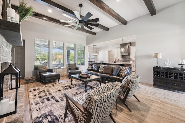 living room with a stone fireplace, beam ceiling, light wood-style flooring, and a ceiling fan