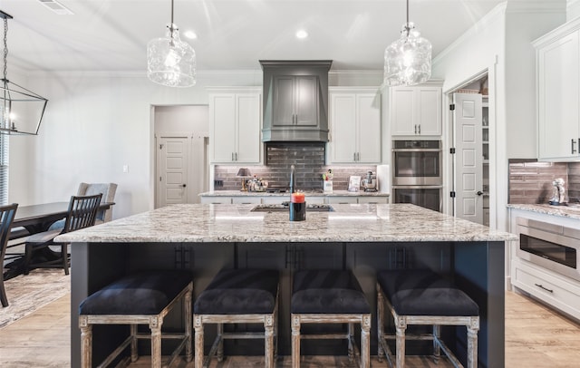 kitchen featuring a chandelier, appliances with stainless steel finishes, a breakfast bar area, and premium range hood