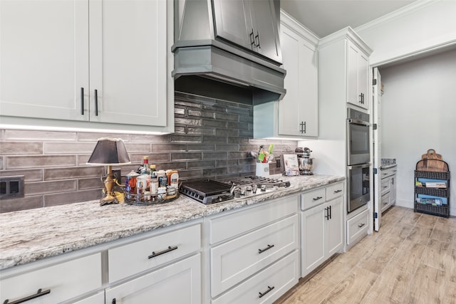 kitchen featuring light wood-style flooring, ornamental molding, stainless steel appliances, wall chimney range hood, and backsplash