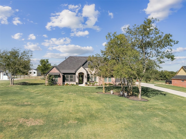 french country home with fence, roof with shingles, a front lawn, stone siding, and brick siding