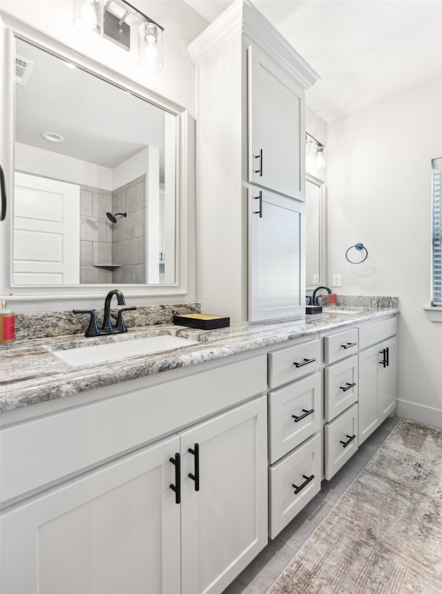 bathroom featuring a sink, baseboards, double vanity, and a tile shower