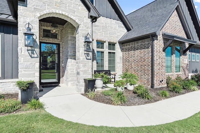 doorway to property featuring stone siding, roof with shingles, board and batten siding, and brick siding