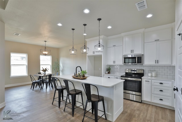 kitchen with a center island with sink, stainless steel appliances, white cabinetry, and light hardwood / wood-style floors