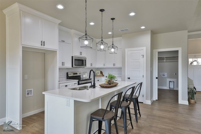 kitchen with hanging light fixtures, stainless steel appliances, white cabinetry, and a kitchen island with sink