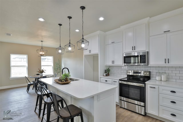 kitchen with white cabinets, pendant lighting, stainless steel appliances, and a center island with sink