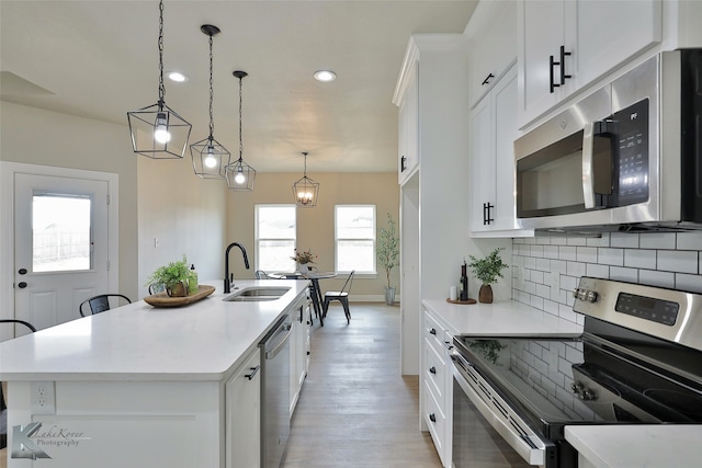 kitchen featuring a kitchen island with sink, appliances with stainless steel finishes, sink, and hanging light fixtures