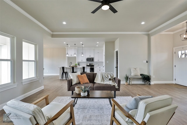 living room featuring light wood-type flooring, ornamental molding, sink, and ceiling fan