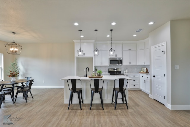 kitchen with pendant lighting, appliances with stainless steel finishes, light hardwood / wood-style floors, a kitchen island with sink, and white cabinetry