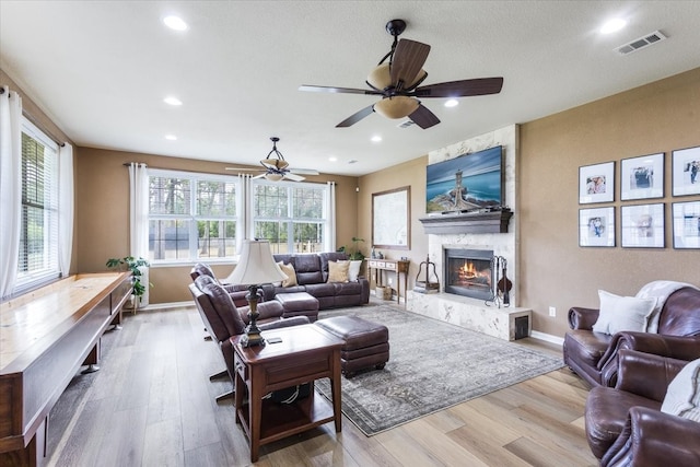 living room with ceiling fan, a wealth of natural light, a fireplace, and light hardwood / wood-style flooring