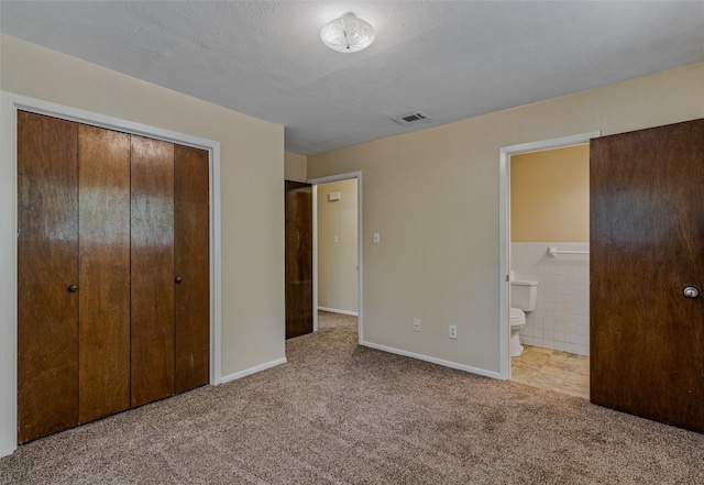 unfurnished bedroom featuring a textured ceiling, light colored carpet, connected bathroom, and a closet