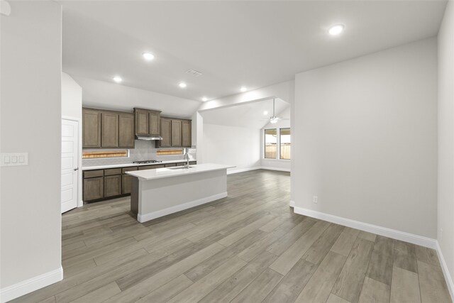 kitchen with stainless steel gas stovetop, a center island with sink, sink, decorative backsplash, and light wood-type flooring