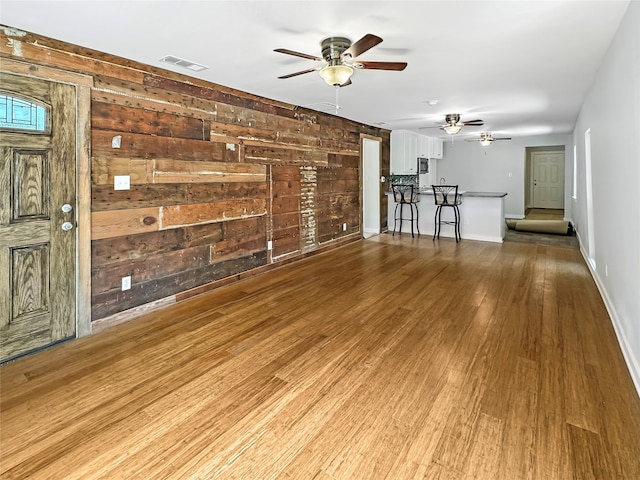 unfurnished living room with wooden walls, hardwood / wood-style floors, and ceiling fan