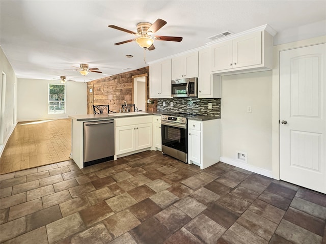 kitchen with appliances with stainless steel finishes, white cabinets, backsplash, kitchen peninsula, and ceiling fan