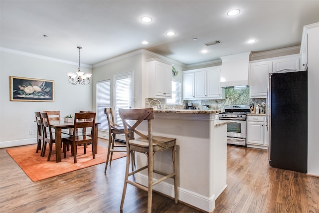 kitchen with white cabinets, hardwood / wood-style flooring, stainless steel range with gas stovetop, premium range hood, and black fridge