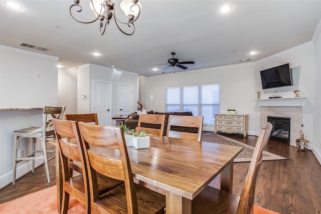 dining room featuring a tiled fireplace, ceiling fan with notable chandelier, dark hardwood / wood-style floors, and ornamental molding