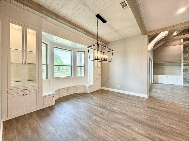 unfurnished dining area with an inviting chandelier, wood-type flooring, and beam ceiling