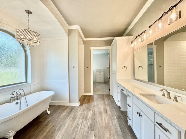 bathroom featuring a tub to relax in, vanity, wood-type flooring, ornamental molding, and a chandelier