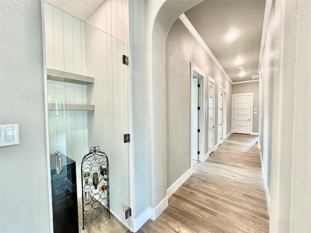 hall with light wood-type flooring, wooden walls, crown molding, and a textured ceiling