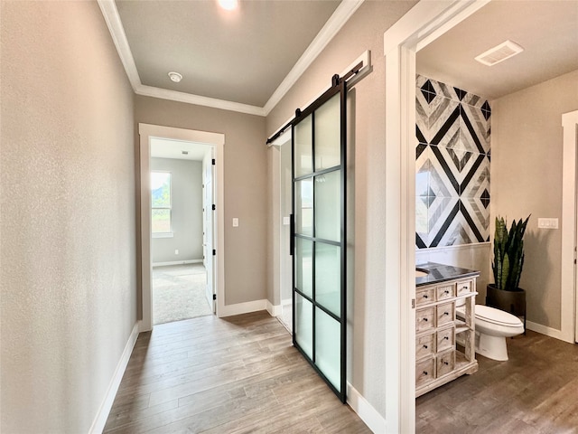 corridor with a barn door, hardwood / wood-style floors, and ornamental molding