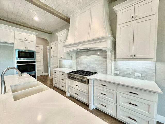 kitchen featuring custom range hood, stainless steel appliances, white cabinetry, sink, and beam ceiling