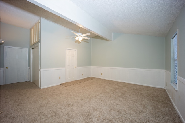 carpeted empty room featuring ceiling fan, lofted ceiling with beams, and a textured ceiling