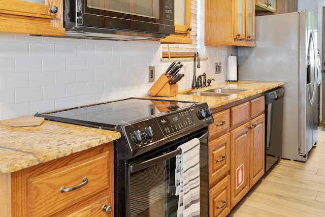 kitchen with light stone counters, sink, light hardwood / wood-style flooring, decorative backsplash, and black appliances