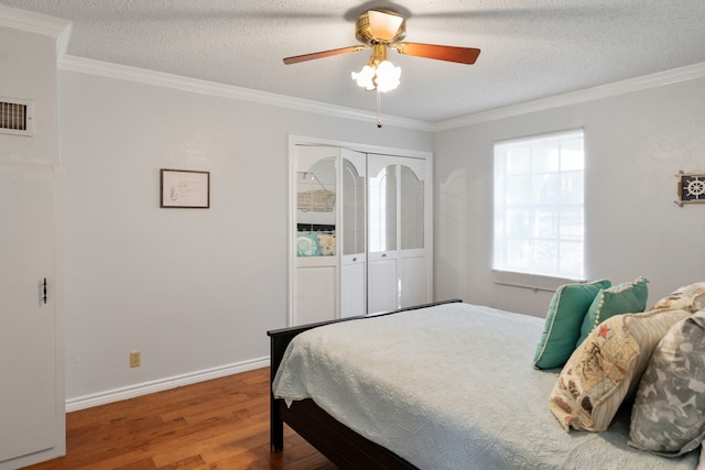 bedroom with a closet, a textured ceiling, ceiling fan, ornamental molding, and hardwood / wood-style floors