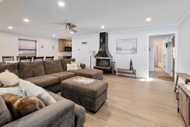 living room with ornamental molding, ceiling fan, light hardwood / wood-style flooring, and a wood stove