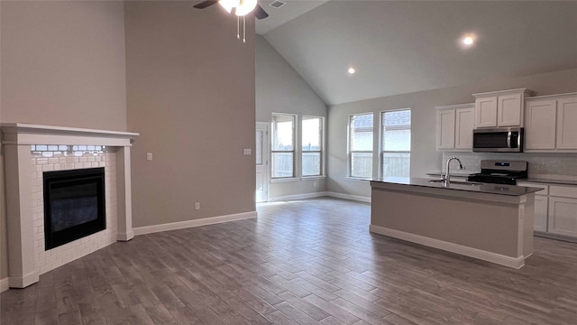 kitchen featuring dark wood-type flooring, white cabinetry, appliances with stainless steel finishes, a fireplace, and a kitchen island with sink