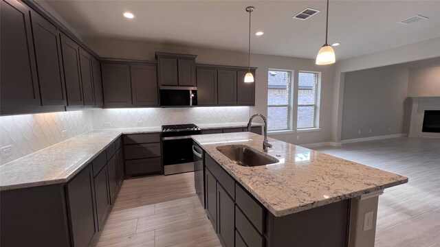 kitchen featuring light stone countertops, decorative light fixtures, tasteful backsplash, sink, and a kitchen island with sink