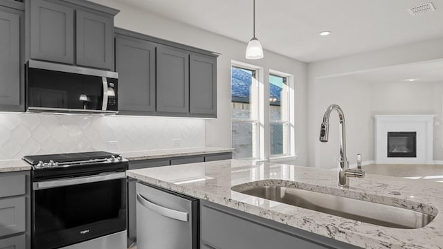 kitchen with sink, gray cabinetry, hanging light fixtures, appliances with stainless steel finishes, and backsplash