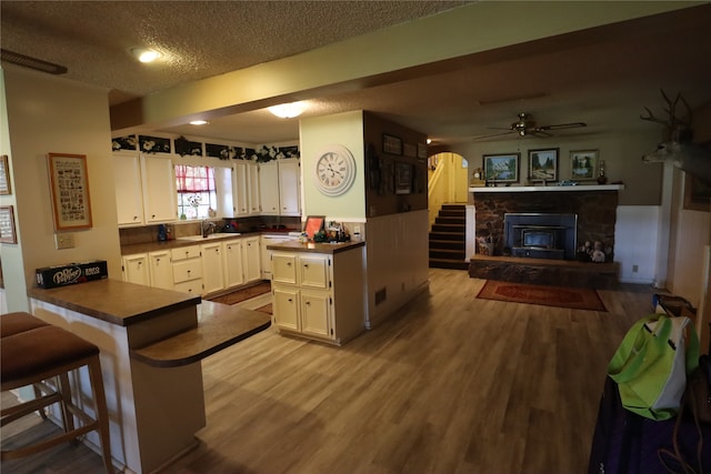 kitchen with ceiling fan, white cabinets, kitchen peninsula, a stone fireplace, and a breakfast bar area