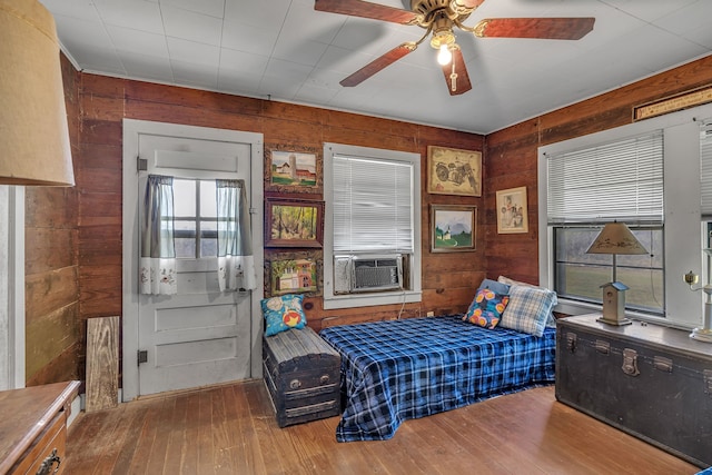 bedroom with wooden walls, ceiling fan, hardwood / wood-style flooring, and cooling unit