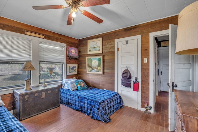 bedroom featuring wood-type flooring, wood walls, and ceiling fan