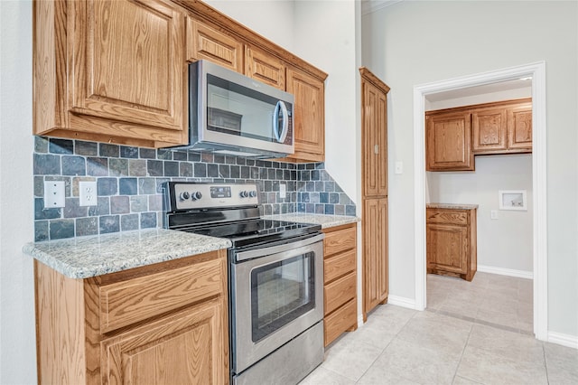 kitchen with appliances with stainless steel finishes, light tile patterned flooring, light stone countertops, and decorative backsplash