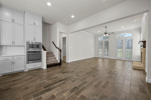 kitchen with ceiling fan, a stone fireplace, white cabinetry, appliances with stainless steel finishes, and dark hardwood / wood-style floors