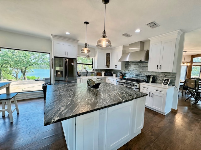 kitchen featuring appliances with stainless steel finishes, a healthy amount of sunlight, white cabinets, and wall chimney range hood