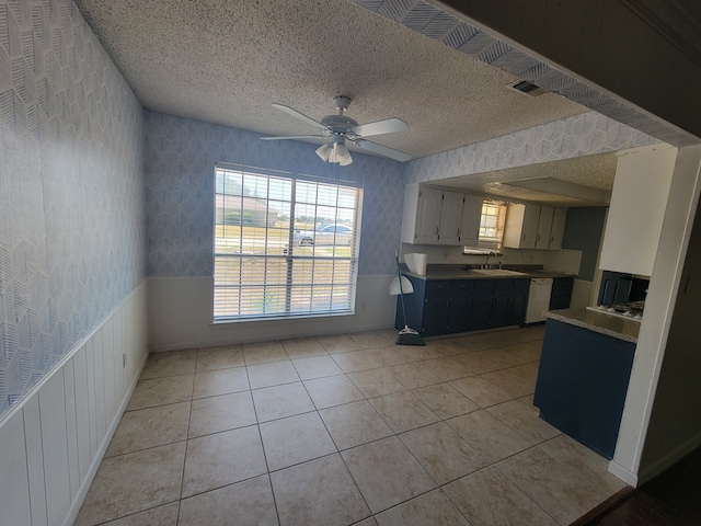 interior space with a textured ceiling, white dishwasher, light tile patterned floors, ceiling fan, and white cabinets