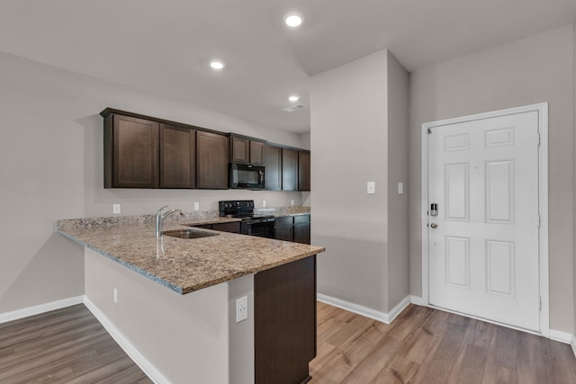 kitchen featuring light hardwood / wood-style floors, black appliances, light stone counters, kitchen peninsula, and dark brown cabinetry