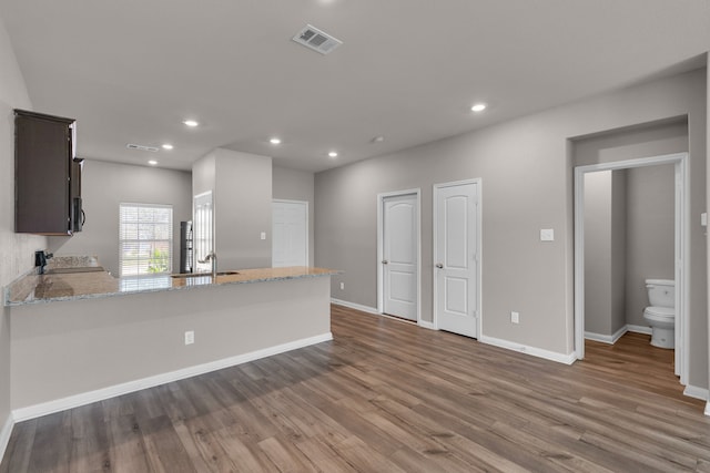 kitchen featuring light hardwood / wood-style flooring, light stone countertops, black appliances, kitchen peninsula, and dark brown cabinetry