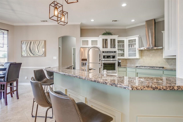 kitchen with pendant lighting, wall chimney exhaust hood, stainless steel appliances, backsplash, and crown molding