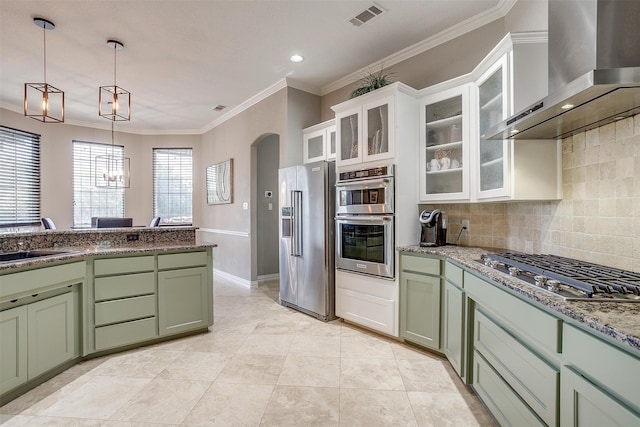 kitchen with white cabinets, tasteful backsplash, green cabinetry, wall chimney exhaust hood, and stainless steel appliances