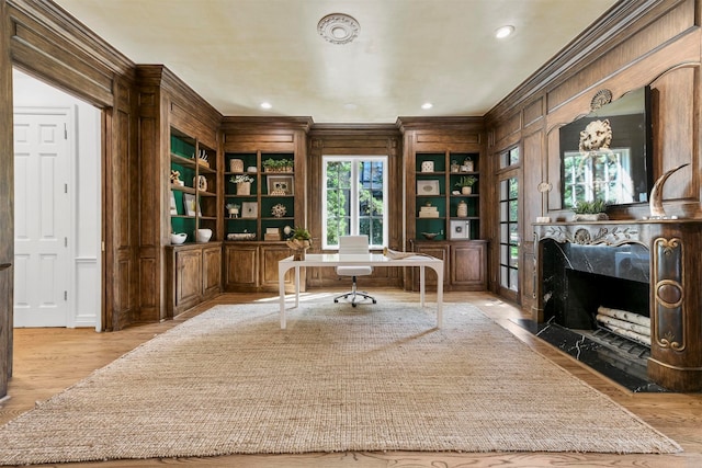 home office with light wood-type flooring, wooden walls, a high end fireplace, crown molding, and built in features