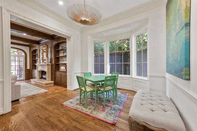 dining space featuring built in features, beam ceiling, light hardwood / wood-style floors, and ornamental molding