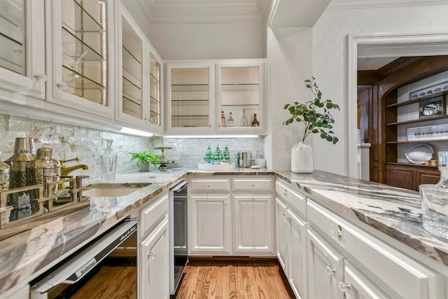 interior space featuring light wood-type flooring, white cabinetry, tasteful backsplash, dishwasher, and light stone counters